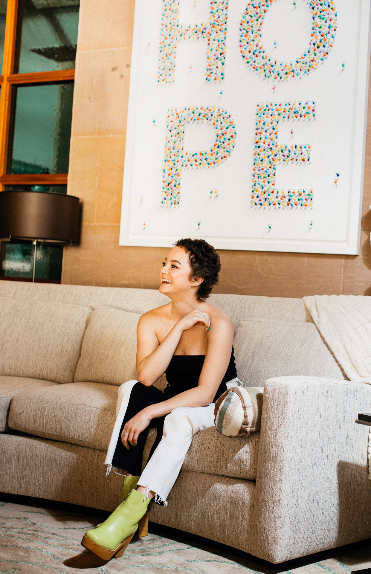 Kasey laughing on a couch beneath a HOPE artwork